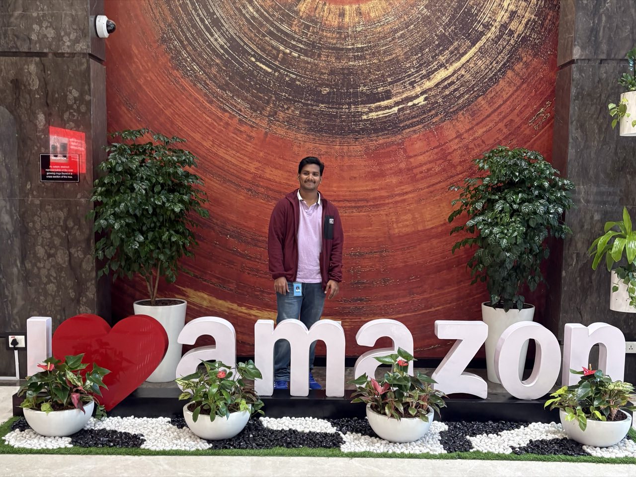 Moinuddin Shaik at the Amazon office in Bengaluru, wearing a visitor badge, standing behind the lobby's I-heart-amazon lettering